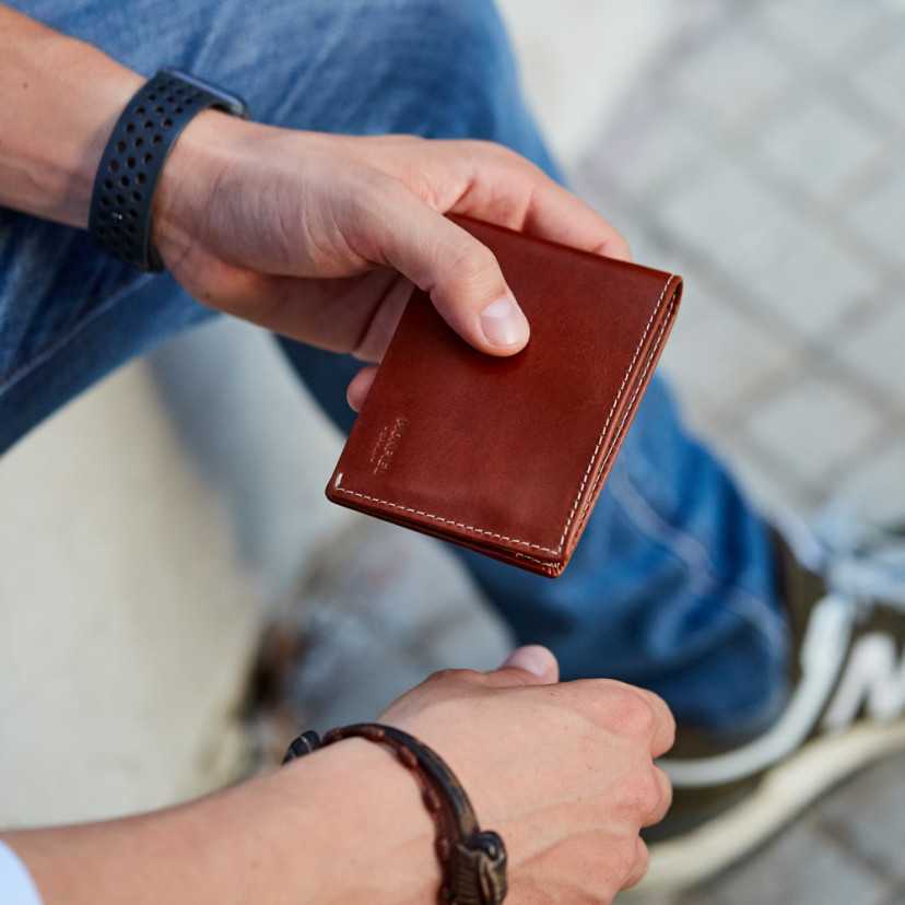 Men’s Havana leather wallet, outdoor shot, held with ground background - MONPIEL