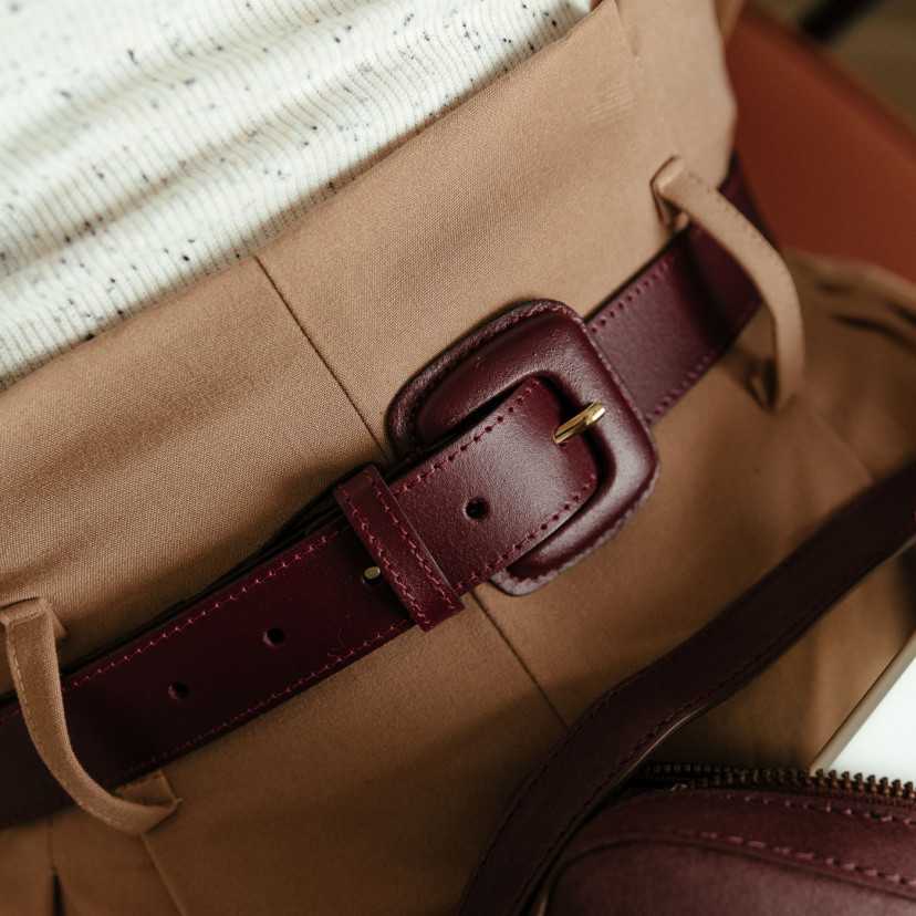 Cinto feminino de couro bordô com fivela revestida, detalhe da fivela usada sobre calça marrom - MONPIEL