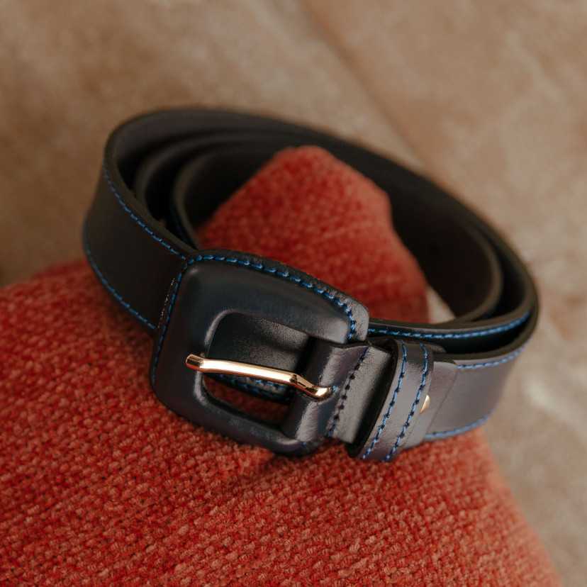 Women’s navy leather belt with covered buckle, coiled on a cushion - MONPIEL