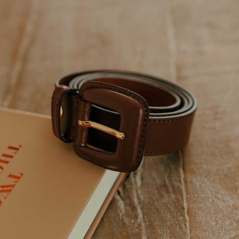 Women’s brown leather belt with covered buckle, coiled on a book - MONPIEL
