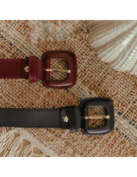 Burgundy and black leather women’s belt with covered buckle, close-up of buckle detail on a rug - MONPIEL Burgundy and black leather women’s belt with covered buckle, close-up of buckle detail on a rug - MONPIEL
