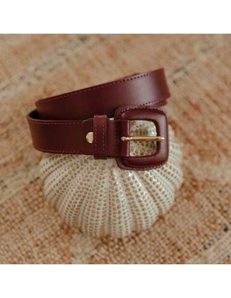 Burgundy leather women’s belt with covered buckle coiled on a decorative object - MONPIEL Burgundy leather women’s belt with covered buckle coiled on a decorative object - MONPIEL