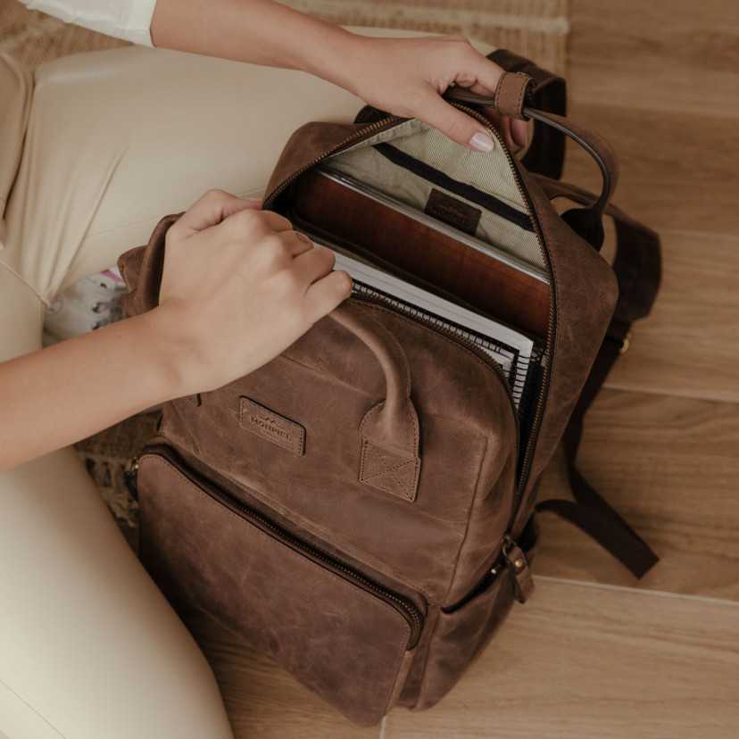 Brown leather backpack being opened on the ground, showing the interior - MONPIEL