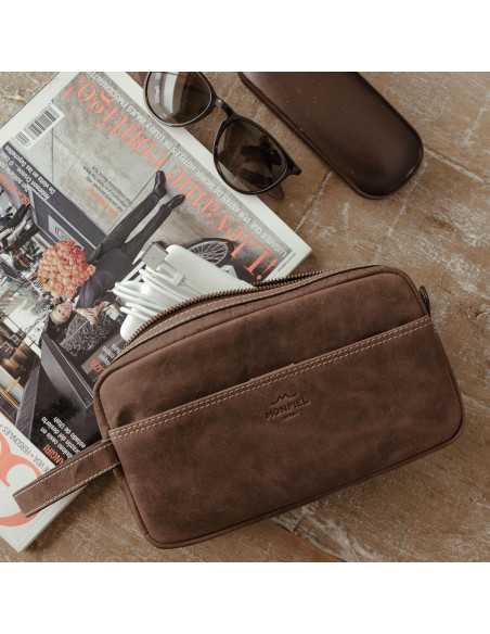 Brown leather men’s toiletry bag, front view slightly tilted with open zipper and pocket, resting on a magazine - MONPIEL