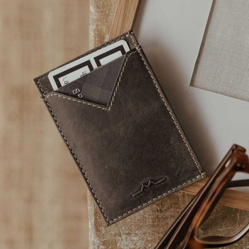 Men’s blue leather cardholder, slightly tilted, resting on a photo frame - MONPIEL