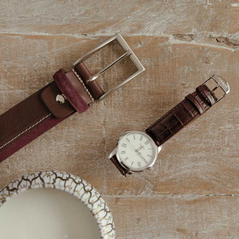 Burgundy leather and suede belt, buckle detail, next to a watch on a table - MONPIEL