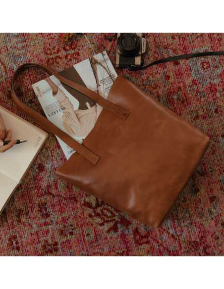 Bolsa shopper em couro, vista frontal e levemente inclinada, apoiada sobre um tapete com detalhe de câmera - MONPIEL