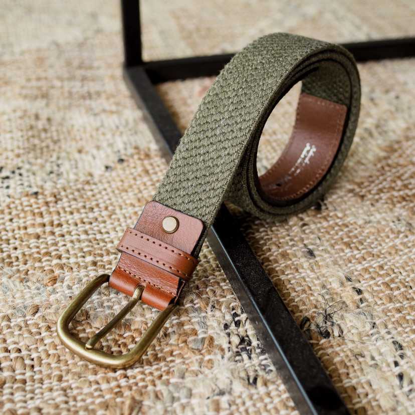 Men’s green elastic leather belt, coiled, with buckle detail, resting on a rug - MONPIEL