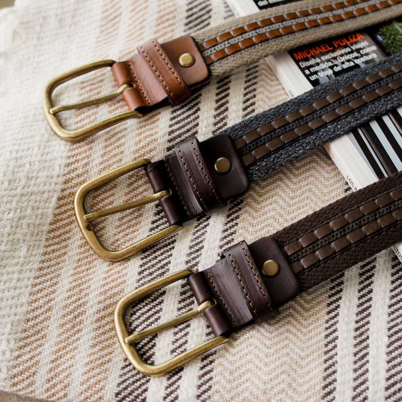 Men’s canvas and leather belts in navy, brown, and green, focusing on the buckle, resting on a blanket - MONPIEL