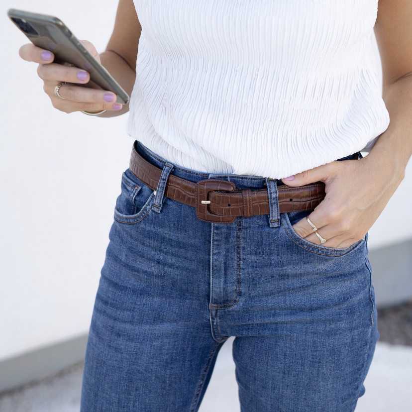 Cinto feminino marrom com fivela revestida e padrão croco, usado na cintura sobre jeans - MONPIEL