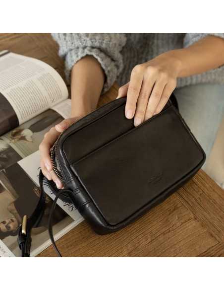 Black leather crossbody bag, front view slightly tilted, resting on a magazine - MONPIEL Black leather crossbody bag, front view slightly tilted, resting on a magazine - MONPIEL