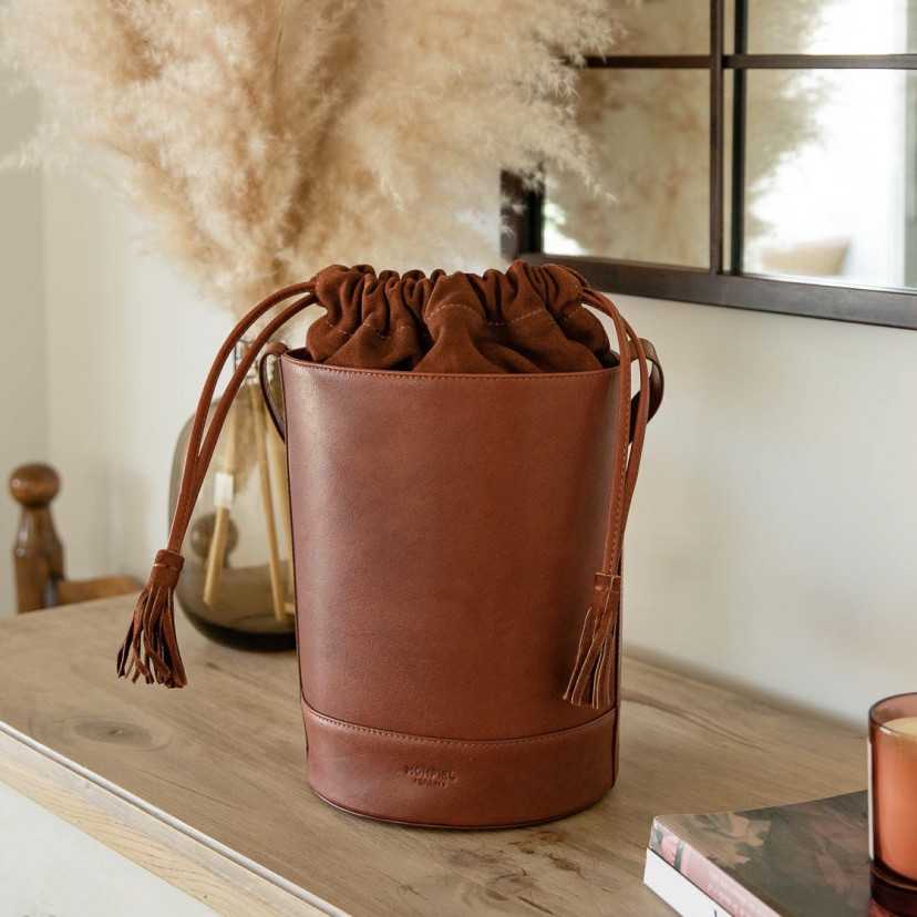 Bolsa redonda em forma de cubo de cor havana, vista frontal apoiada sobre um móvel, com espelho ao fundo - MONPIEL