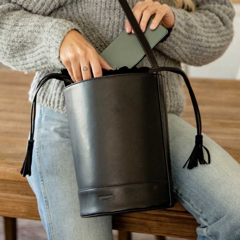 Bolsa redonda em forma de cubo em preto, vista frontal colocando um celular - MONPIEL