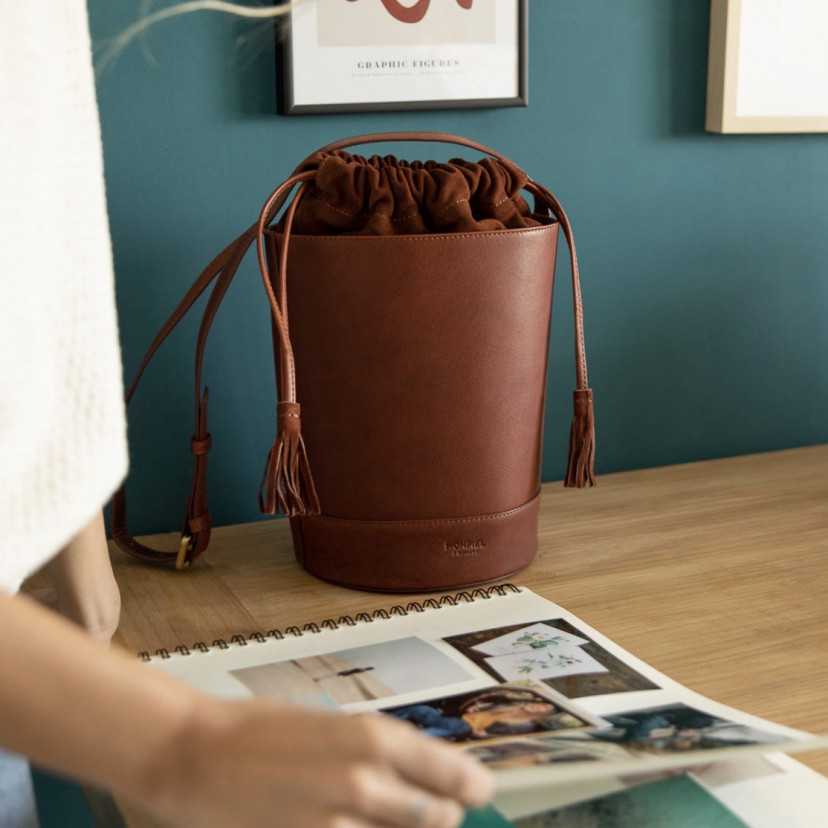Bolsa redonda em forma de cubo de couro havana, vista frontal em frente a uma parede - MONPIEL