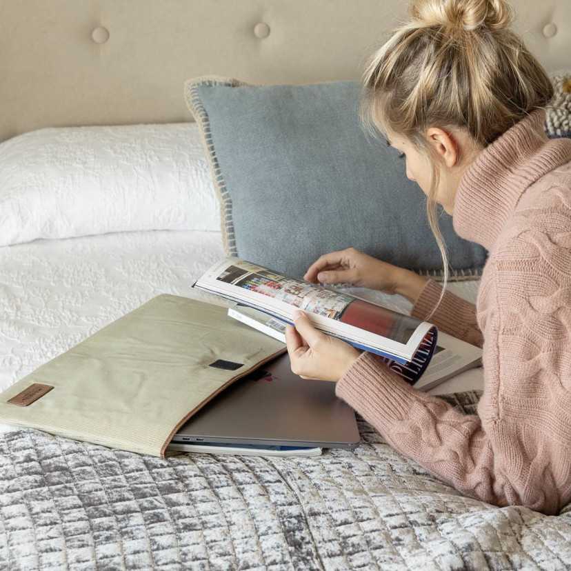 Capa para notebook de 15" polegadas na cor bege sobre uma cama com a modelo lendo uma revista - MONPIEL