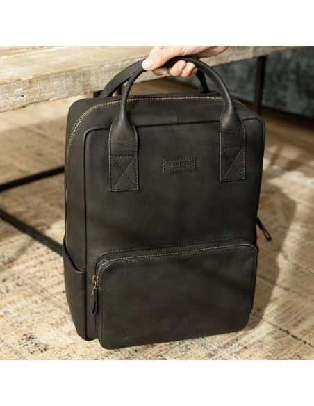Black leather backpack held by the short handles, resting on a rug - MONPIEL