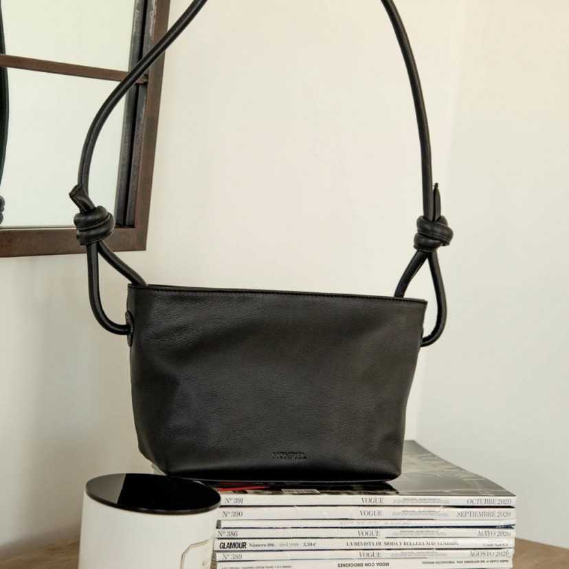 Bolsa pequena de couro preta com nós, vista frontal, detalhes das alças, apoiada sobre revistas - MONPIEL