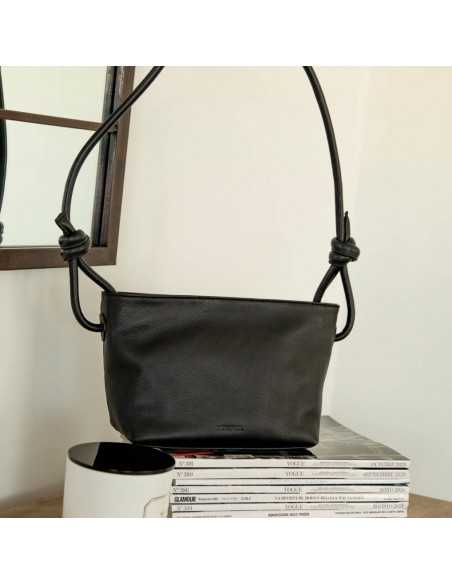 Small black leather knotted bag, front view with handle details, resting on magazines - MONPIEL Small black leather knotted bag, front view with handle details, resting on magazines - MONPIEL