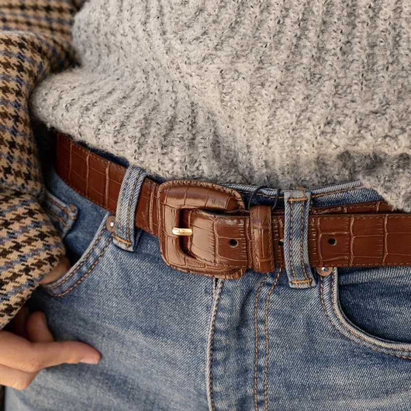 Women’s brown crocodile-patterned covered-buckle belt, worn at the waist over jeans, focus on the buckle - MONPIEL