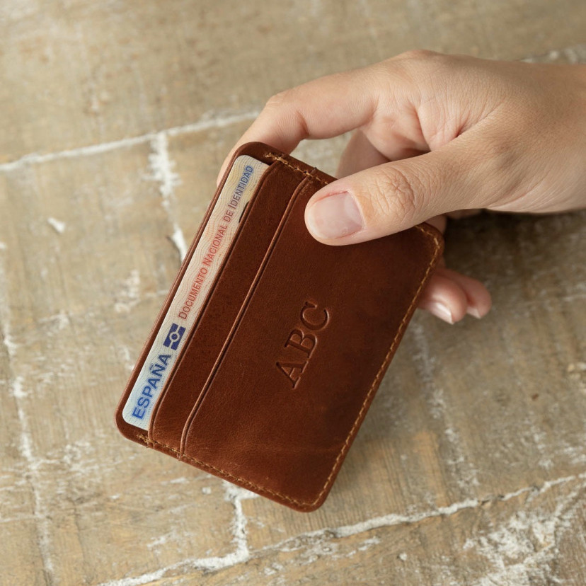 Mini leather cardholder in Havana, shown from the front with personalization detail in hand on a table background - MONPIEL