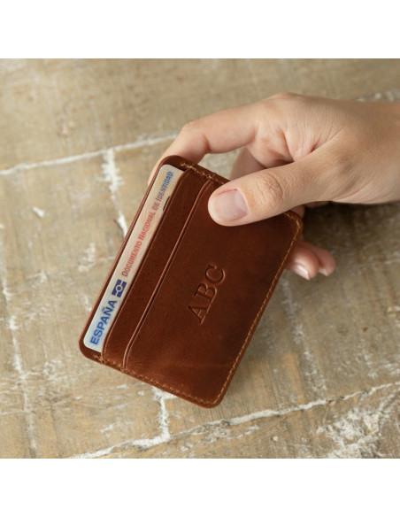 Mini leather cardholder in Havana, shown from the front with personalization detail in hand on a table background - MONPIEL Mini leather cardholder in Havana, shown from the front with personalization detail in hand on a table background - MONPIEL