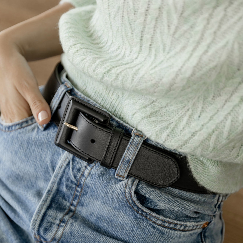Wide women's leather belt with covered buckle in black, worn over jeans with focus on the buckle - MONPIEL