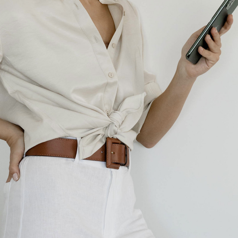 Wide women's leather belt with covered buckle in tan, shown in perspective over white linen pants - MONPIEL