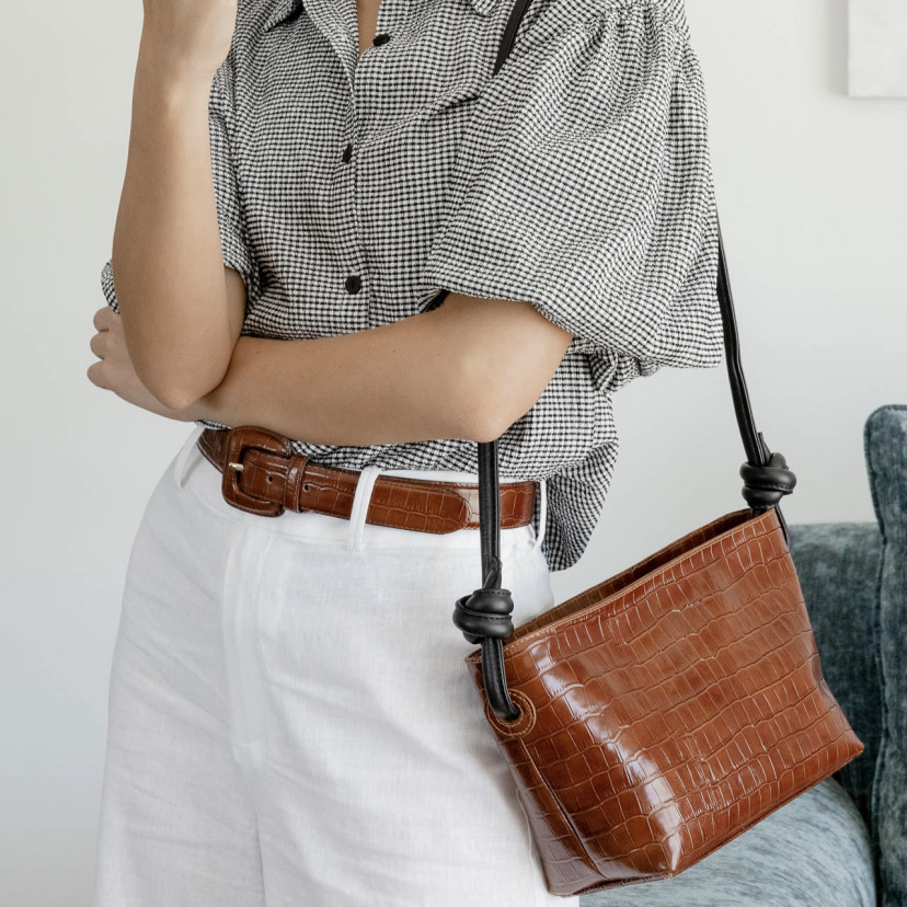 Women's belt with covered buckle and crocodile print in brown, worn over white pants, shown in perspective with a matc - MONPIEL