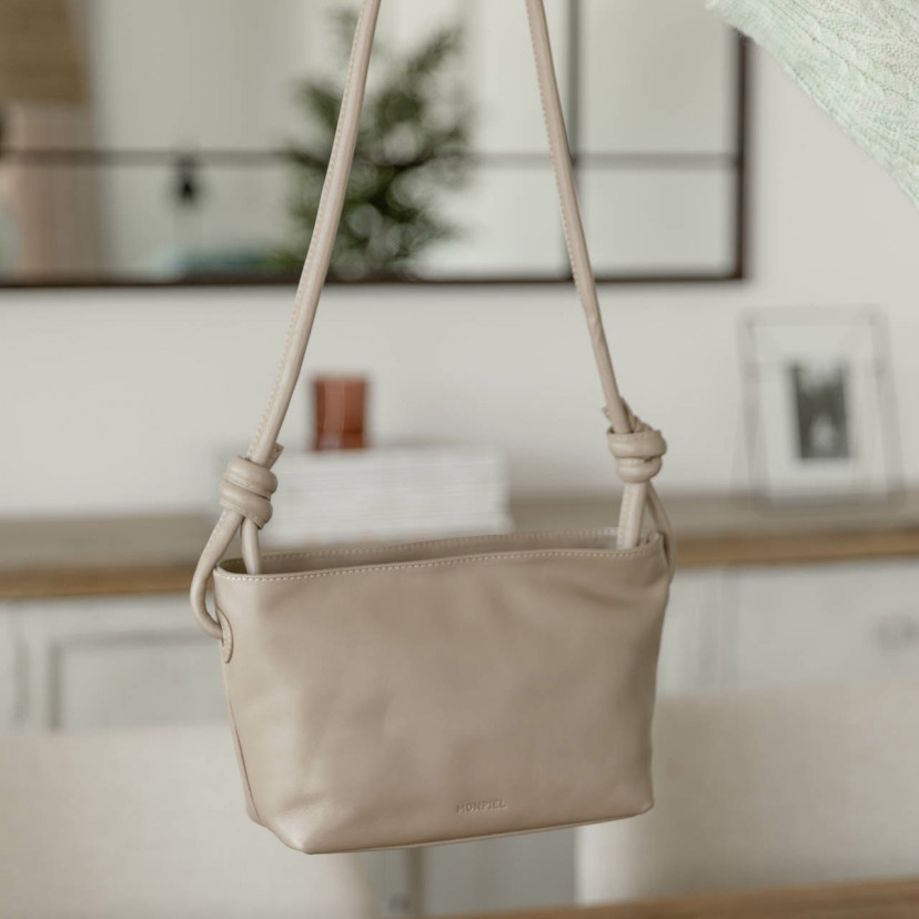 Bolsa pequena de couro com nós na cor taupe com vista frontal segurada pela alça - MONPIEL
