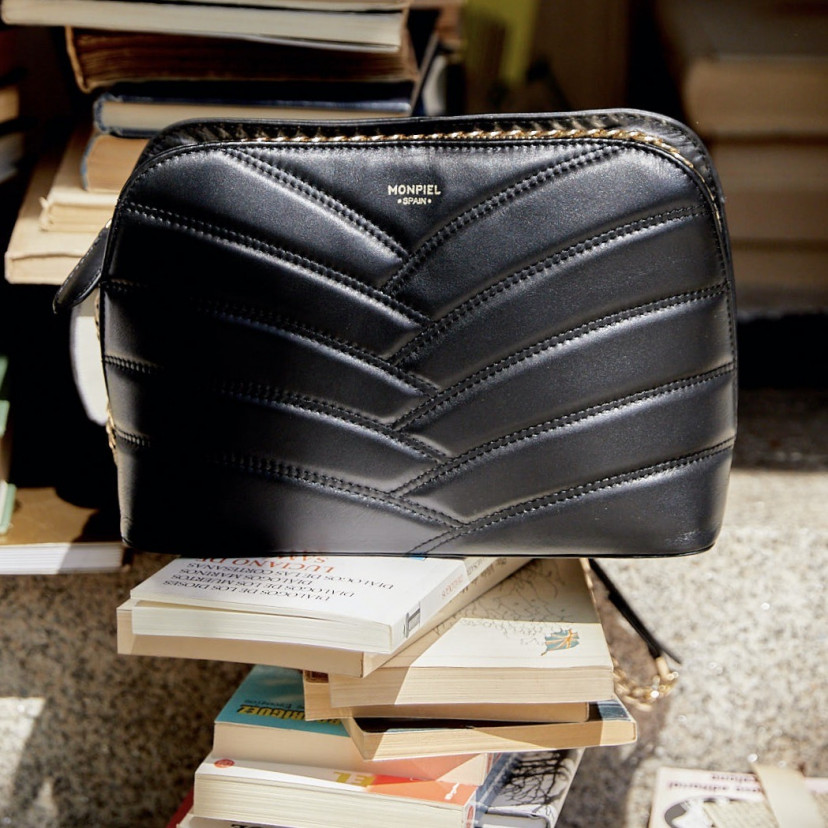 Black leather quilted bag with gold chain, shown from the front resting on books - MONPIEL
