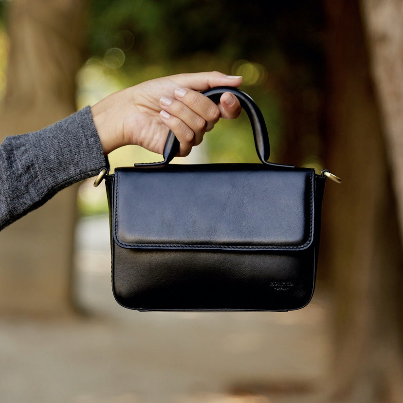 Bolsa de couro pequena Armado na cor preta com alça curta segurada em primeiro plano focado, fundo externo - MONPIEL