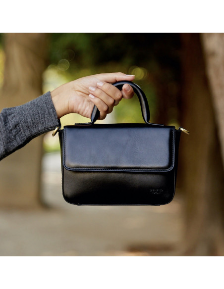Bolsa de couro pequena Armado na cor preta com alça curta segurada em primeiro plano focado, fundo externo - MONPIEL Bolsa de couro pequena Armado na cor preta com alça curta segurada em primeiro plano focado, fundo externo - MONPIEL