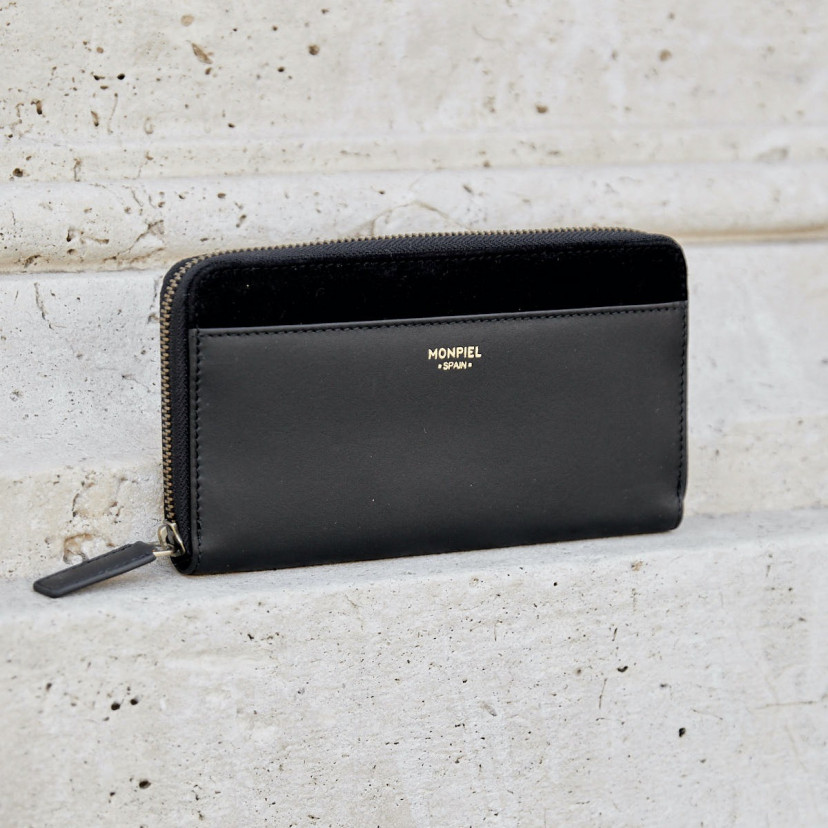 Women's leather zipper wallet in black, shown from the front against a wall - MONPIEL