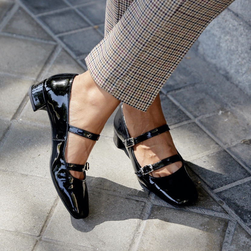 Black patent leather Mary Janes Lolina, with crossed legs outdoors - MONPIEL