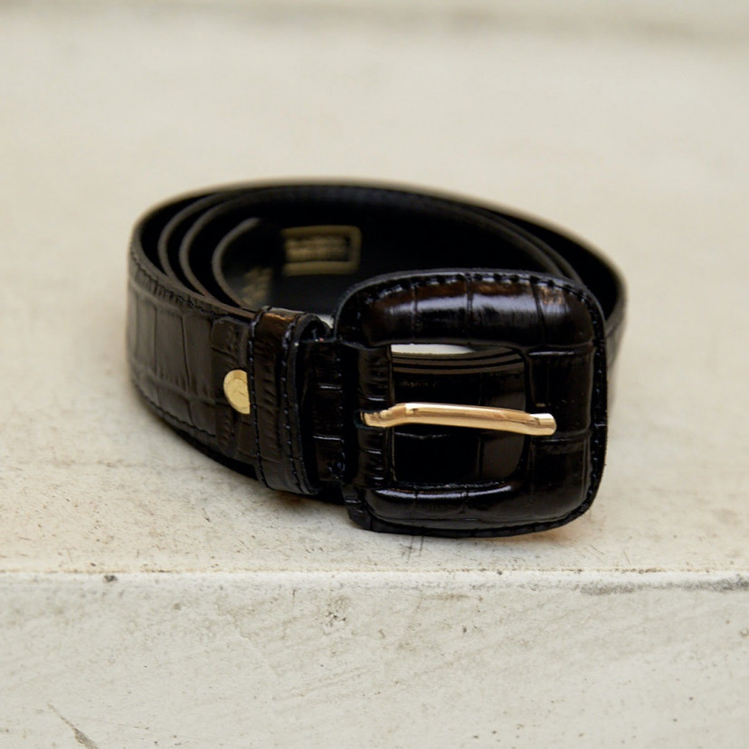 Women's belt with covered buckle and crocodile print in black, coiled on a wall with focus on the buckle detail - MONPIEL