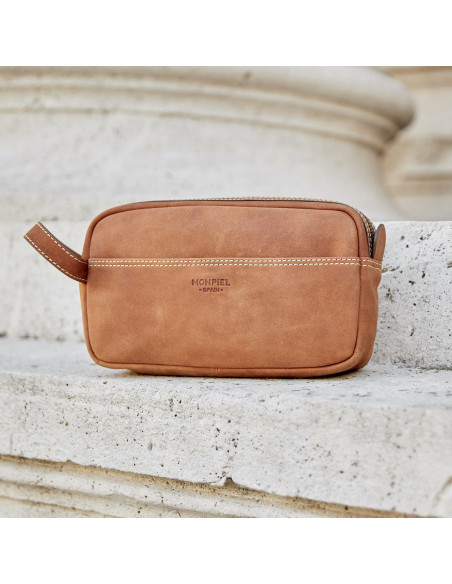 Necessaire masculino em couro Havana com vista frontal e detalhes das costuras, foto externa apoiada em um muro - MONPIEL Necessaire masculino em couro Havana com vista frontal e detalhes das costuras, foto externa apoiada em um muro - MONPIEL
