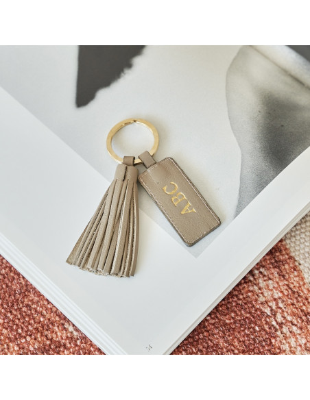 Chaveiro com franjas de couro na cor taupe com iniciais personalizadas sobre uma revista - MONPIEL Chaveiro com franjas de couro na cor taupe com iniciais personalizadas sobre uma revista - MONPIEL