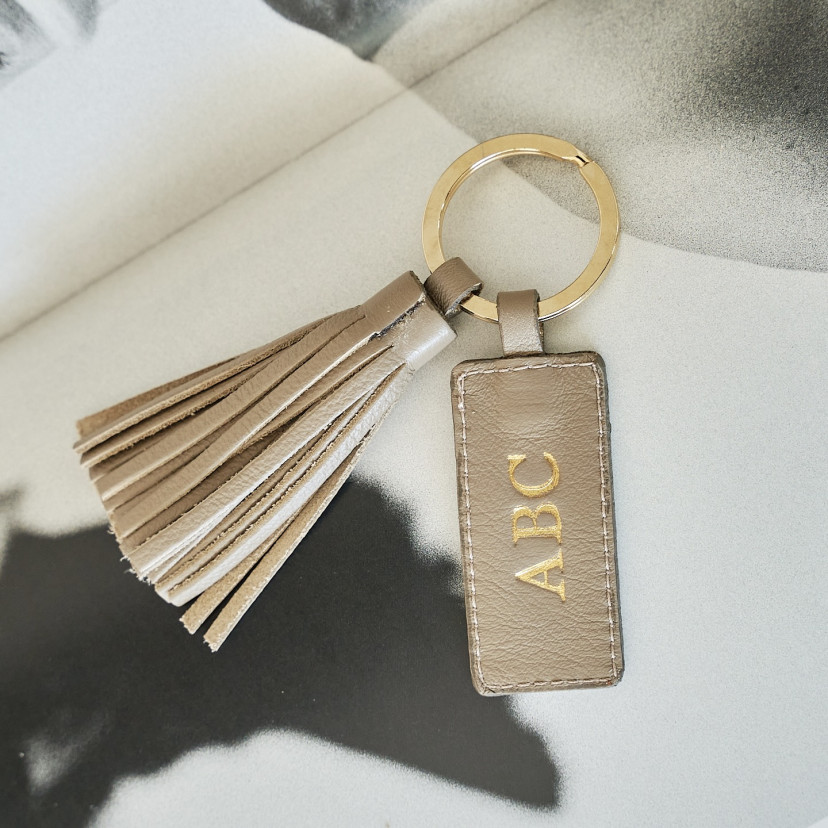Taupe leather tassel keychain with personalized initials, shown in close-up detail - MONPIEL