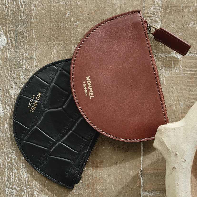 Black and brown half-moon leather coin purses, resting on a wooden table - MONPIEL