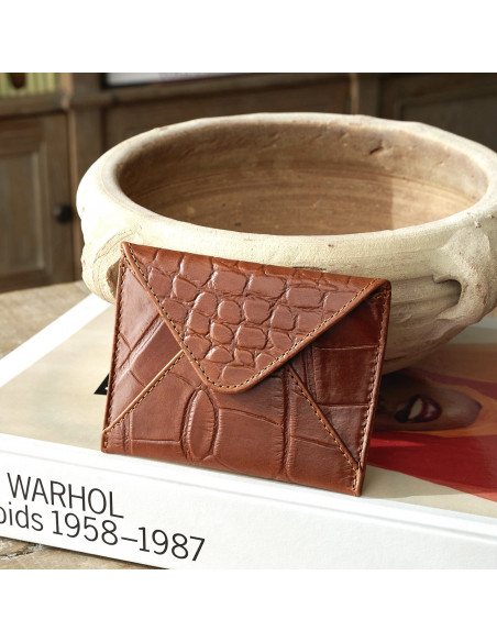 Porta-cartões de envelope em couro na cor couro apoiado sobre livro e cerâmica - MONPIEL