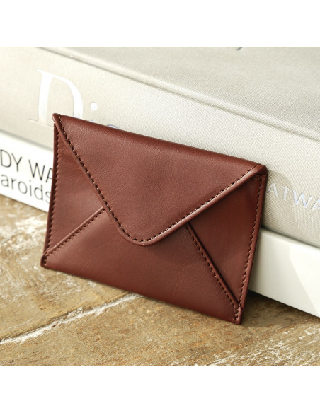 Porte-cartes en cuir en forme d'enveloppe marron reposant sur des livres sur une table en bois - MONPIEL Porte-cartes en cuir en forme d'enveloppe marron reposant sur des livres sur une table en bois - MONPIEL