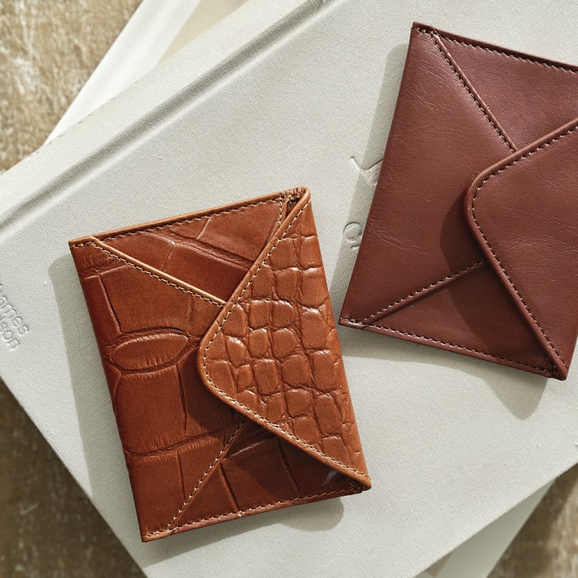 Leather envelope cardholder in brown and tan, resting on a book, shown from above - MONPIEL