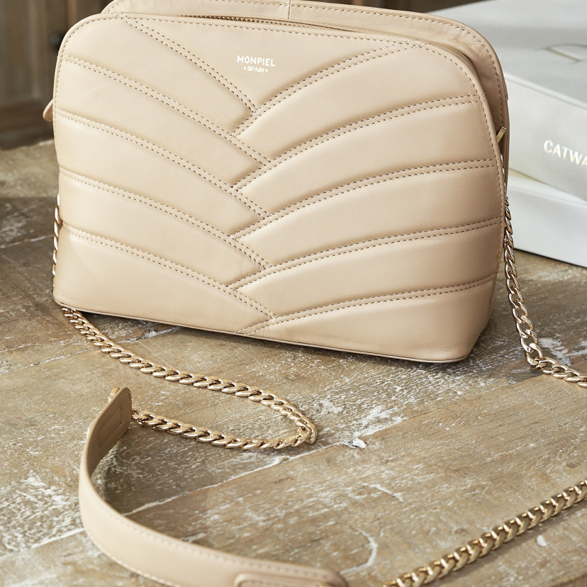 Beige leather quilted bag with gold chain, placed on a wooden table - MONPIEL