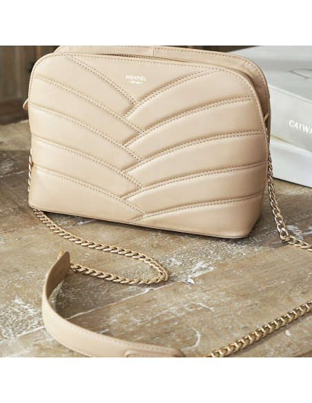 Quilted leather bag with gold chain in beige placed on a wooden table - MONPIEL Quilted leather bag with gold chain in beige placed on a wooden table - MONPIEL