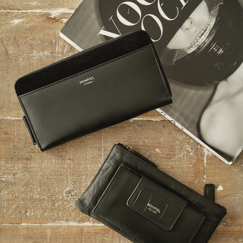 Women's leather zipper wallet in black, resting on a table with a magazine in the background - MONPIEL