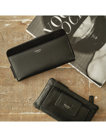 Women's leather zipper wallet in black, resting on a table with a magazine in the background - MONPIEL