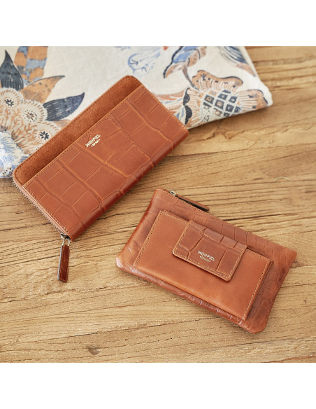 Cartera mujer de piel cremallera en color cuero inclinada sobre mesa de madera y revista - MONPIEL Cartera mujer de piel cremallera en color cuero inclinada sobre mesa de madera y revista - MONPIEL