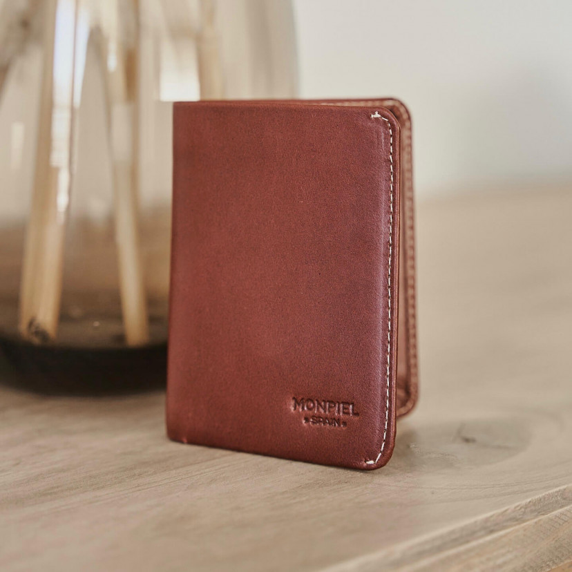 Small Havana leather men's wallet with billfold, resting on a table with a vase in the background - MONPIEL