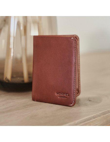 Portefeuille pour homme en cuir petit avec porte-billets, couleur havane, sur une table avec un vase derrière - MONPIEL Portefeuille pour homme en cuir petit avec porte-billets, couleur havane, sur une table avec un vase derrière - MONPIEL