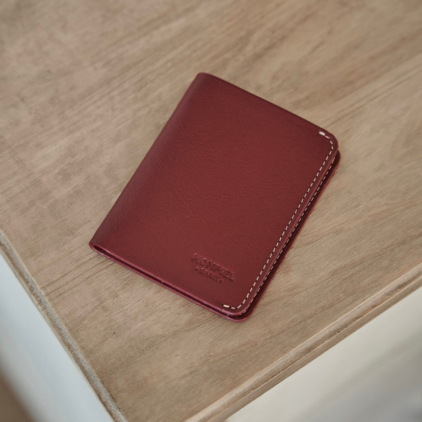 Small burgundy leather men's wallet with billfold, shown from the front and tilted on a table - MONPIEL